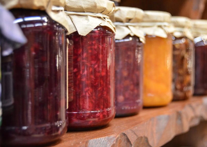 Homemade jam in jars on a timber shelf.