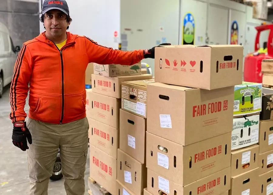 Mohammad standing next to a pallet of CERES Fair Food grocery orders, packed into boxes and ready to be delivered.