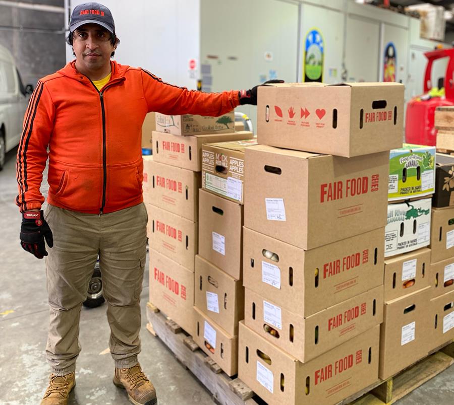 Mohammad standing next to a pallet of CERES Fair Food grocery orders, packed into boxes and ready to be delivered.
