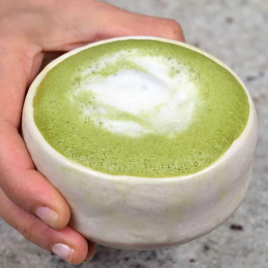 A hand holding a green, frothy matcha latte